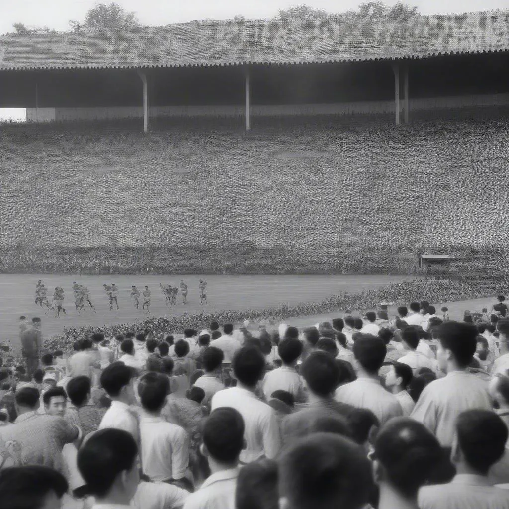 Bóng đá Việt Nam năm 1954: Một bức ảnh đen trắng, ghi lại hình ảnh một trận đấu bóng đá ở Việt Nam vào năm 1954, với khán giả cổ vũ cuồng nhiệt.